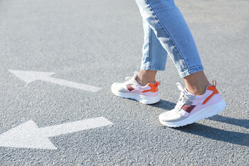 Wall Mural - Choice of way. Woman walking to drawn mark on road, closeup. White arrows pointing in different directions