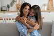 © DimaBerlin - Cute girl child cuddling smiling mother, sitting together on sofa in living room. Portrait of happy family mom and teen daughter hugging looking at camera while spending leisure time at home