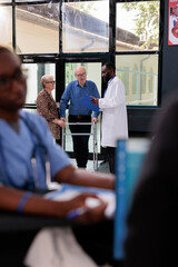 Wall Mural - Practitioner doctor discussing illness symptoms with injured elderly patient before start medical consultation. Old man with walking frame having appointment in hospital waiting lobby