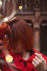 Wall Mural - Close up woman hiding face in hair on street portrait picture. Closeup side view photography with old city on background. High quality photo for ads, travel blog, magazine, article