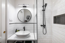 Modern Bathroom In Black And White Style With High-quality Expensive Fittings. White Brick Walls And Sink On Countertop Are Matched With Black Faucets Framed In Mirror And Decorative Elements.