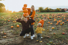 Woman Helping Man In Balancing Jack O' Lanterns On Head By Children In Patch