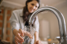 Woman Filling Water From Faucet In Glass At Home