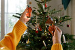 © Westend61 - Hands of woman putting illuminated string lights on Christmas tree at home