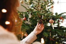 Hand Of Woman Touching Pine Cone Hanging On Christmas Tree At Home
