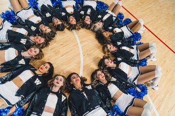 Wall Mural - High angle shot. Cheerleading squad lying on the floor in a circle. Sport concept. High quality photo