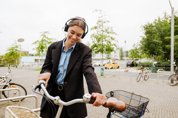 Young joyful woman walking with bicycle through city street
