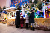Fototapeta Kuchnia - Mother with three children visit Christmas nativity crib scene in church.