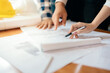 © Nutchapong Wuttisak - architect or engineer help brainstorm ideas and are meeting together with partners for structural design and model construction Pointing to the blueprint on the table in the workplace.