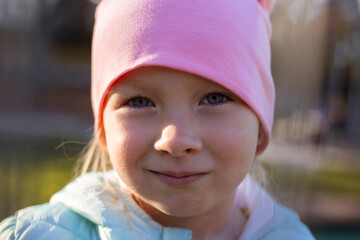 Wall Mural - Smiling cute preschool girl child in a jacket in a pink cap on the street