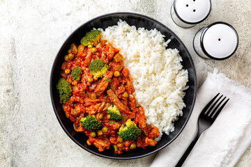 Wall Mural - Plate with beef and vegetable  stew, green peas, broccoli, tomato sauce with white rice. Black plate. Top view.