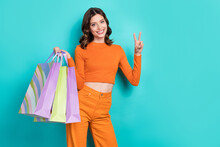 Photo Of Adorable Glad Lady Shopaholic Shopper Wear Orange Outfit V-sign Cool Choice Clothes Empty Space Isolated On Cyan Color Background