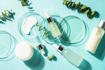 Poster - Cosmetic laboratory concept . Glass petri dish with cosmetic products and serum bottles at blue background. Flat lay image.
