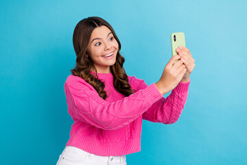 Poster - Photo of young funny schoolgirl teenager cute kid wear pink pullover hold smartphone take shot online video call isolated on blue color background