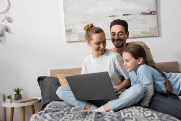 Wall Mural - positive parents and happy kid looking at laptop in bedroom.