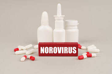 On a gray surface are pills, white jars and a red wooden block with the inscription - Norovirus