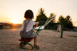 back view of one small caucasian toddler child sitting alone on the seesaw in park in sunset lonely with no friends copy space childhood growing up concept social issues rejected