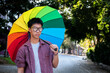 Portrait young asian boy wears rainbow wristband and holding rainbow umbrella on street, concept for being assertive in presenting your true LGBT identity to today's society is accepted by society.