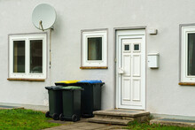 Plastic Trash Cans Near The Entrance To A Residential Building. Satellite Dish On The Wall Above The Window