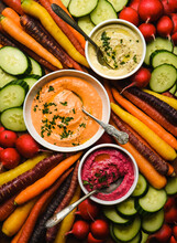 Bowls Of Different Flavoured Hummus And Raw Vegetables For Dipping.