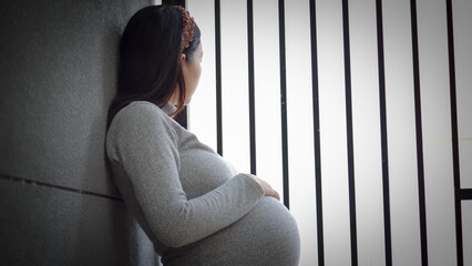 Portrait of mature pregnant woman at home looking outside the fence. Young pregnant woman standing by fence at home and thinking about the future