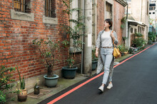 Full Body Of Stylish Positive Young Aged Female In Jeans And Sneakers Strolling Along Old Taiwan Street Near Modern Building At Taipei