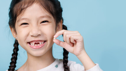 Wall Mural - Asian child's hand shows the fallen out small white milk tooth close-up, Dentistry and Health care concept, Empty space isolated on blue background