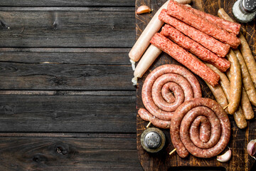 Canvas Print - Different kinds of raw sausages on wooden Board with spices.