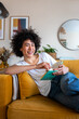 © Daniel - Happy African American woman relaxing at home reading a book sitting on the couch looking at camera. Vertical