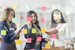 © David - Young creative business Asian woman standing with her colleagues writing new ideas on sticky notes over glass wall, business marketing strategy or User experience ux ui concept.