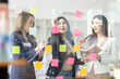 © David - Young creative business Asian woman standing with her colleagues writing new ideas on sticky notes over glass wall, business marketing strategy or User experience ux ui concept.
