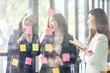 © David - Young creative business Asian woman standing with her colleagues writing new ideas on sticky notes over glass wall, business marketing strategy or User experience ux ui concept.