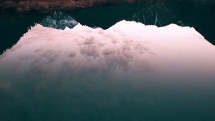 Dark blue mirror color of water in a mountain lake. The smooth surface is like a mirror, trees, yellow-green hills, mountains and the sky are reflected. Tree trunks are standing in the water. Issyk