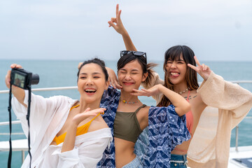 Group of Attractive Asian woman friends using digital camera photography together while travel on luxury private catamaran boat yacht sailing in the ocean on summer holiday vacation at tropical island