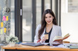 © David - Asian Businesswoman having a tea, sitting on desk in workplace, writing down notes, opened laptop in document the financial report, business plan investment, finance analysis concept.