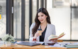 © David - Asian Businesswoman having a tea, sitting on desk in workplace, writing down notes, opened laptop in document the financial report, business plan investment, finance analysis concept.