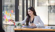© David - Asian Businesswoman having a tea, sitting on desk in workplace, writing down notes, opened laptop in document the financial report, business plan investment, finance analysis concept.