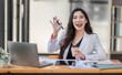 © David - Asian Businesswoman having a tea, sitting on desk in workplace, writing down notes, opened laptop in document the financial report, business plan investment, finance analysis concept.