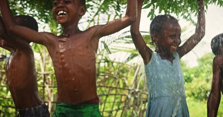 Wall Mural - Group of African Kids Jumping and Laughing when Water Gets Poured on Them. Happy and Innocent Black Children Playing and Enjoying the Blessing of Rain Water After Long Drought. Pan Shot