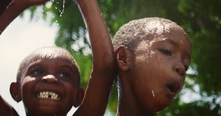 Wall Mural - Close Up on a Group of Happy and Innocent Black Children Playing and Enjoying the Blessing of Rain Water After Long Drought. Authentic African Kids Jumping and Laughing when Water Gets Poured on Them.