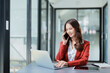 © Jirapong - Portrait of a young Asian woman showing a smiling face as she uses her phone, computer and financial documents on her desk in the early morning hours
