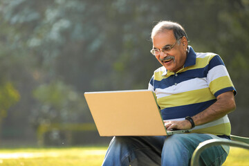 Indian senior man using laptop at park