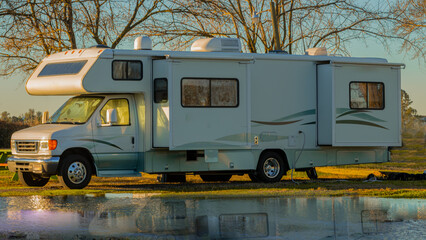rv class c motorhome with slides out parked camping next to water early morning light