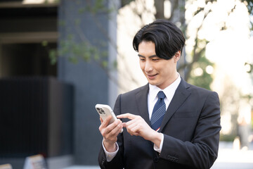 Wall Mural - Asian businessman tapping his phone outside up