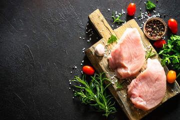 Wall Mural - Turkey fillet steaks with spices and herbs at wooden board at black table. Top view with copy space.