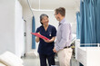 © Austockphoto - smiling middle aged woman wearing blue scrubs holding a file while talking to a man in a clinic ward