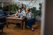 © Cavan Images - Young and mid adult roommates using laptop at table against potted plants in living room