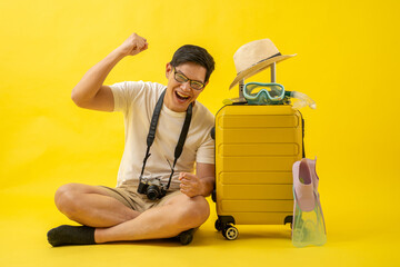 Portrait of happy Asian traveler tourist man with retro camera, hat, snorkel, fins and suitcase isolated on yellow background.