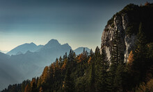 Rock Face With Alpine Forest And Hazy Backdrop In The Distance Revealing The Southern Border Of Austria And Slovenia.