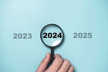 Wall Mural - hand holding black magnifier glass with 2024 year among 2023 and 2025 for preparation and focus new 
